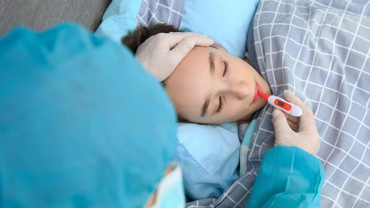Un băiat bolnav stă întins pe pat și i se ia temperatura cu un termometru. În România a fost declarată stare de urgență epidemiologică din cauza gripei