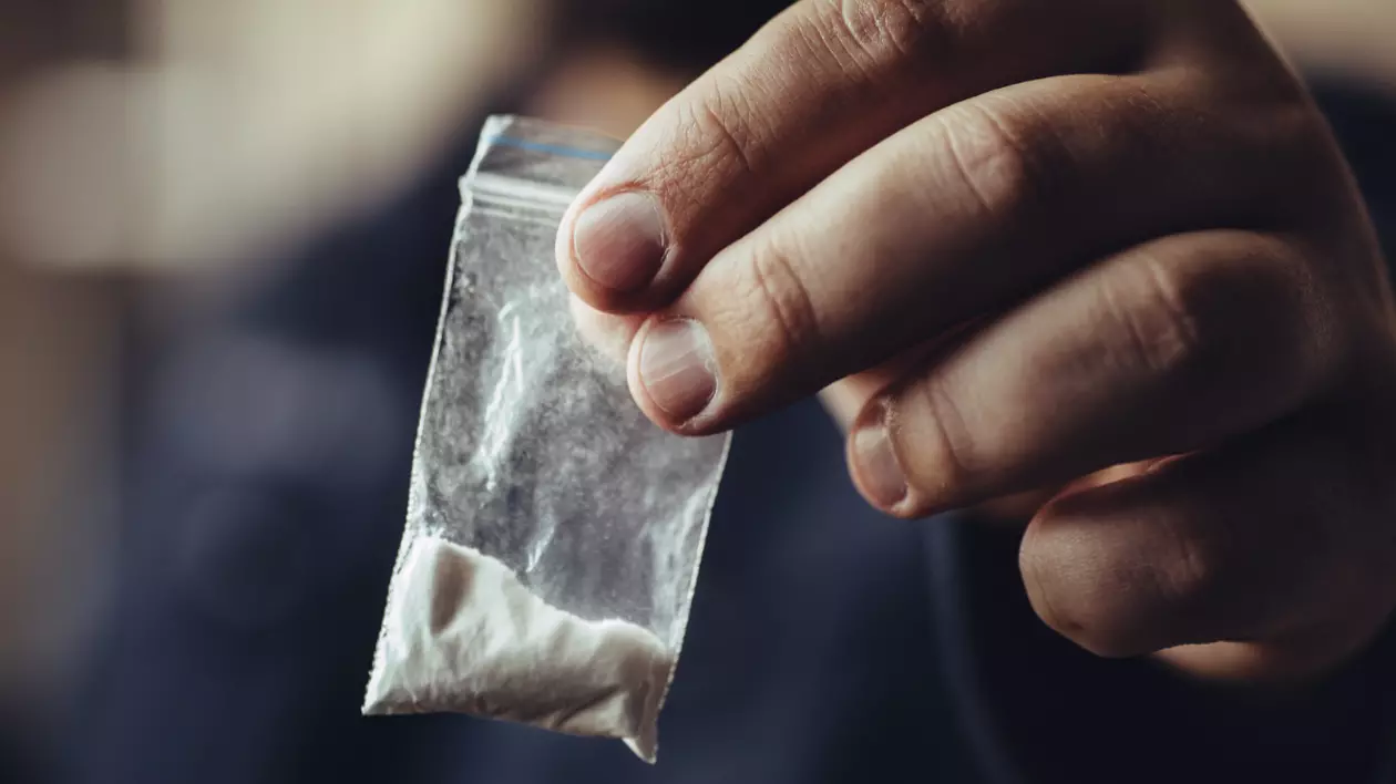 În imagine este ilustrat un bărbat care ține un plic cu droguri în mână